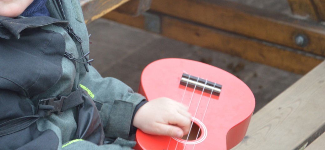 Barn sidder udenfor med en rød ukulele