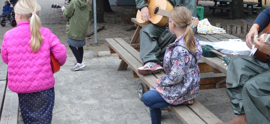 Børn lytter til en mand, der spiller på guitar